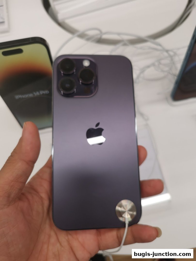 A hand holds a purple iPhone 14 Pro, showcasing its camera and Apple logo.