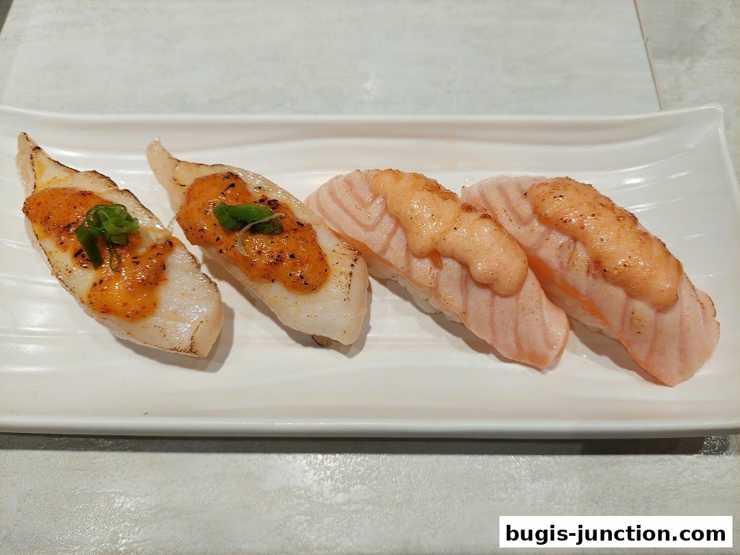 A white plate holds four pieces of sushi, two with white fish and two with salmon.