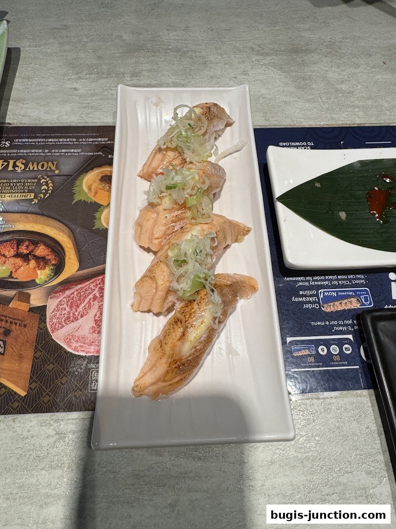 A plate of salmon sushi with green onions and a side dish with sauce.