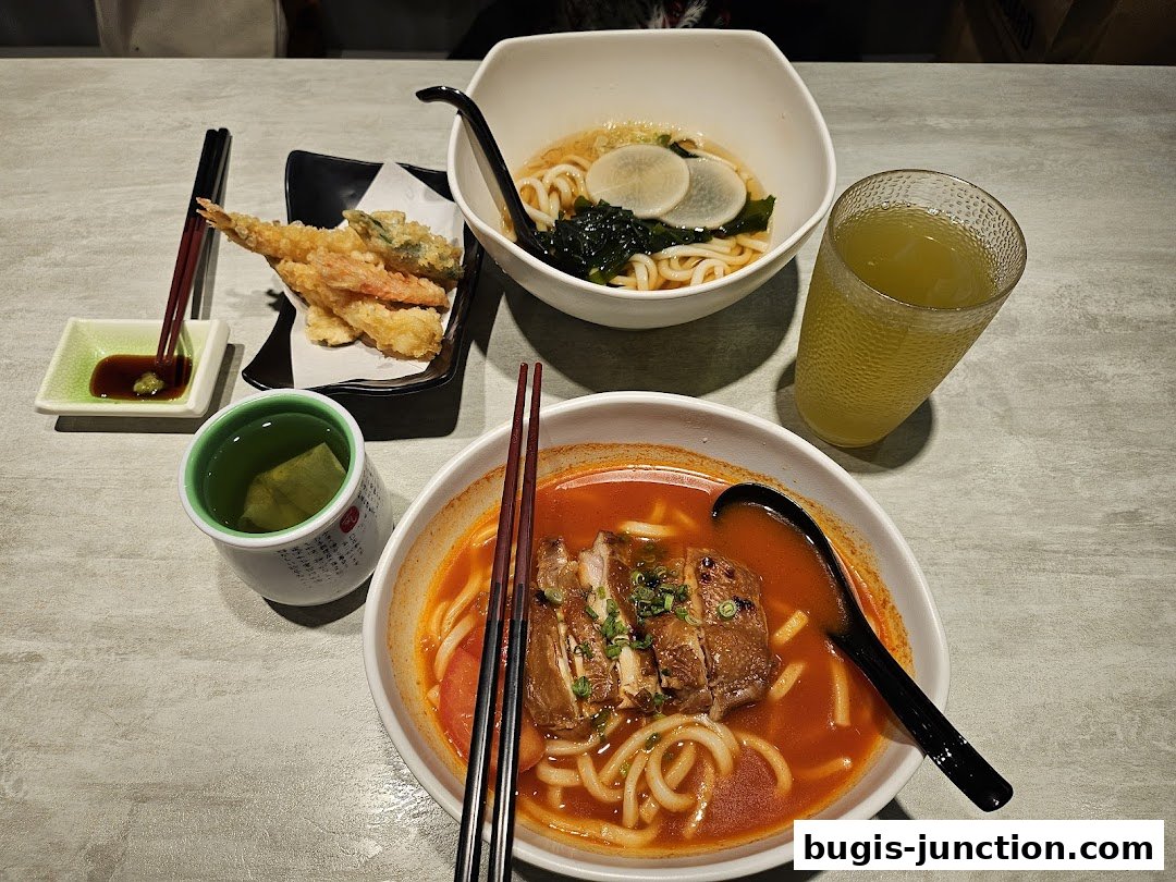 A table setting with two bowls of udon noodles, tempura, and drinks.