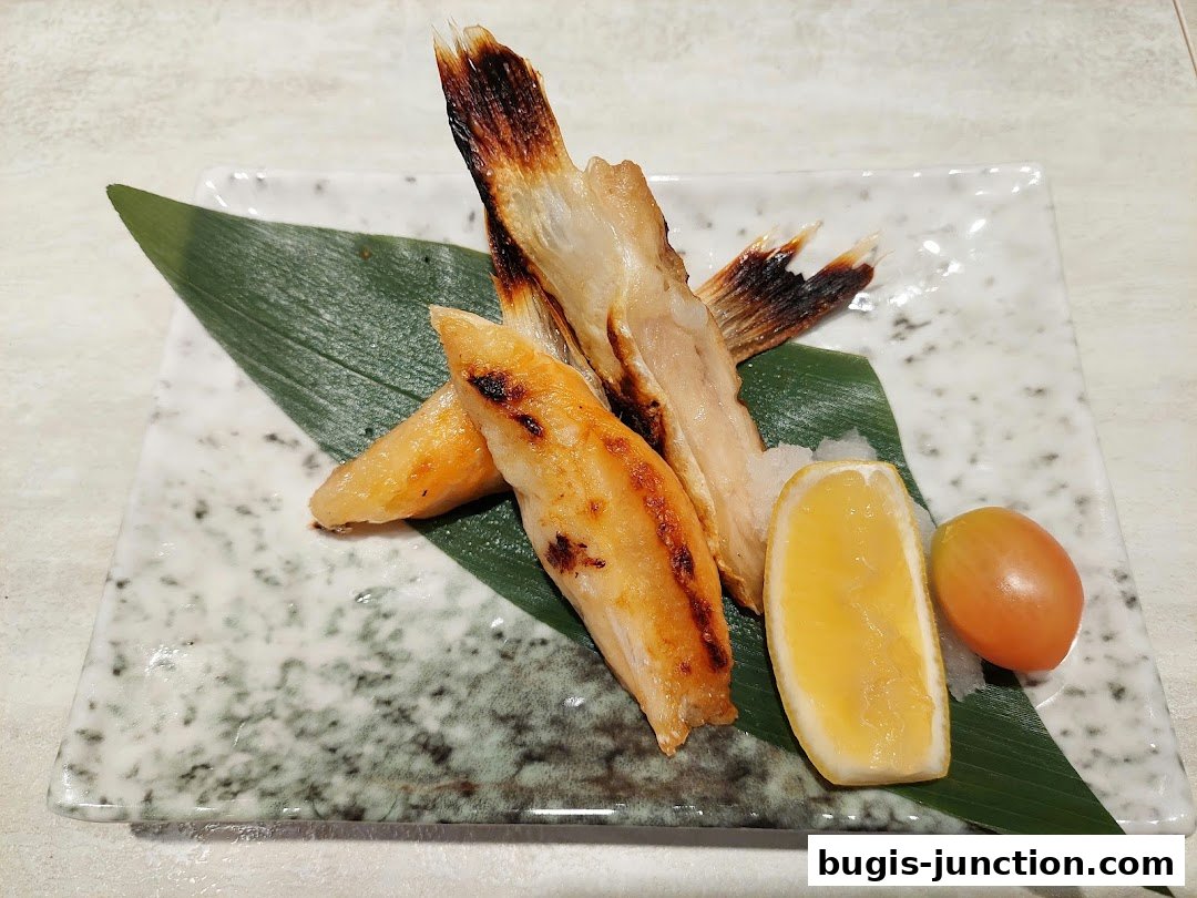 A plate of grilled fish with lemon and tomato, garnished with a leaf.