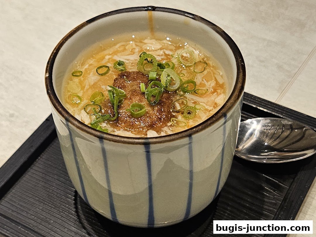 A close-up of a Japanese savory egg custard dish topped with crab and scallions.