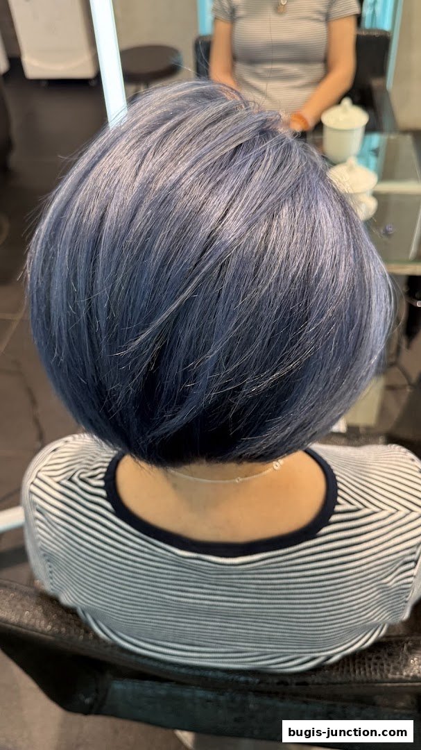A person with a stylish blue bob haircut sitting in a salon chair.