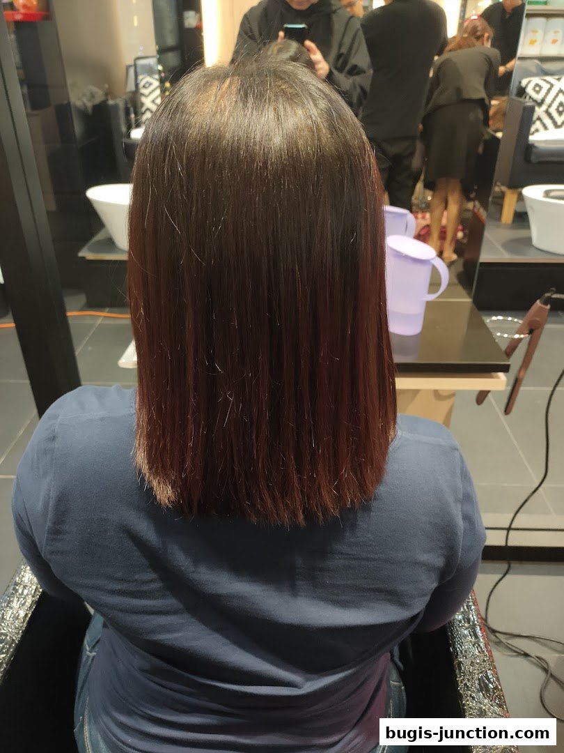 A person's back with freshly cut, dark red hair in a salon.