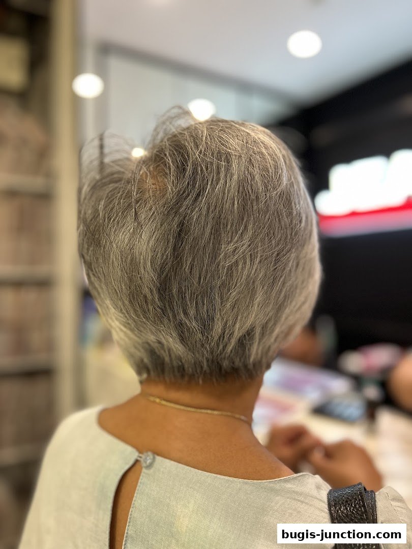 A person's back with short grey hair, viewed from behind in a salon.