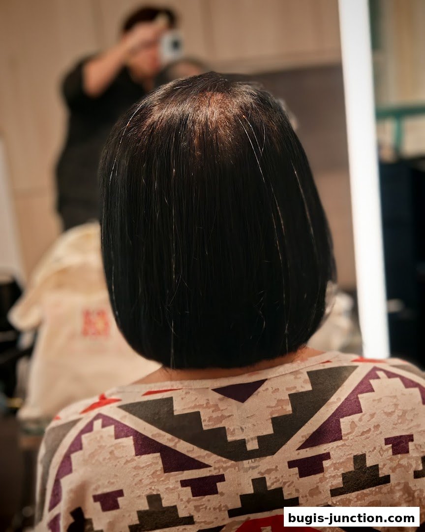 A person's back with dark hair, possibly receiving a hair treatment or styling.