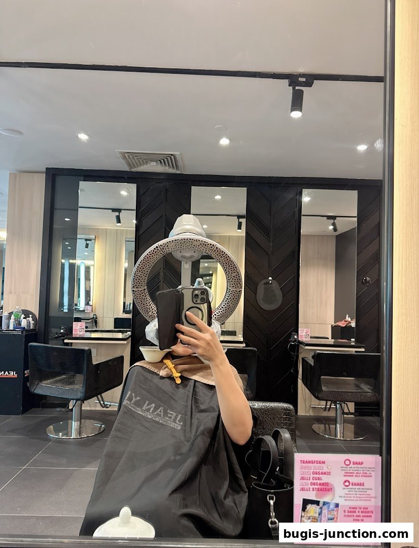 A person sits in a salon chair under a hair dryer, reflecting in a mirror.