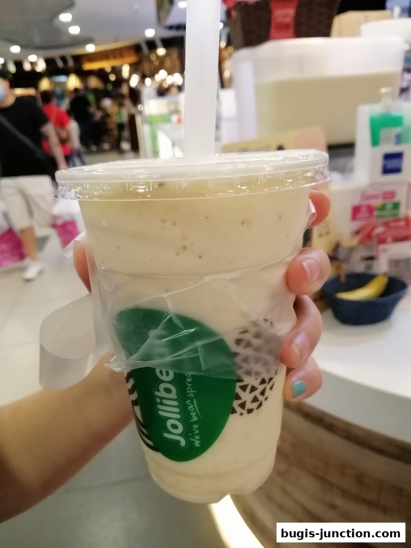 A hand holds a Jollibee beverage with a straw in a clear plastic cup.