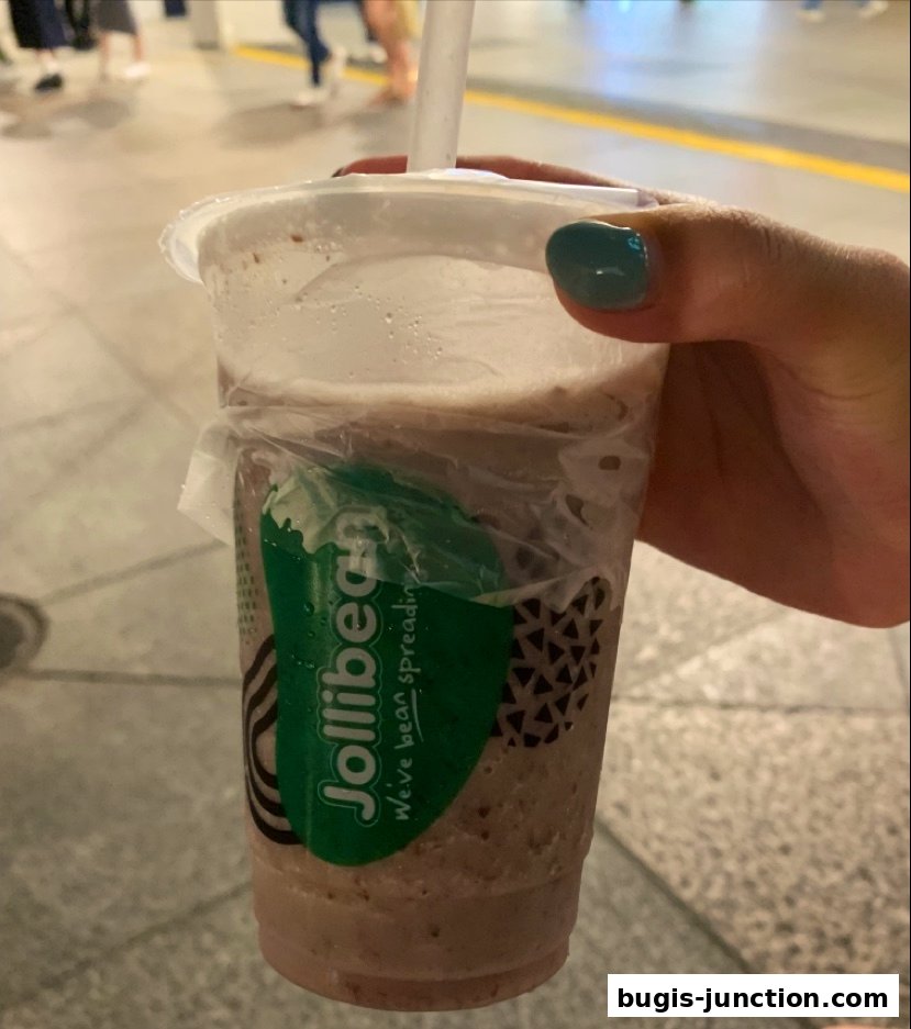 A hand holds a Jollibee drink with a green logo and white straw.