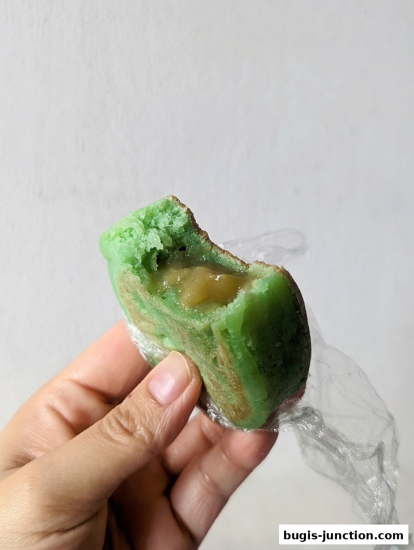 A hand holds a green, bite-sized pastry filled with a sweet, gooey center.