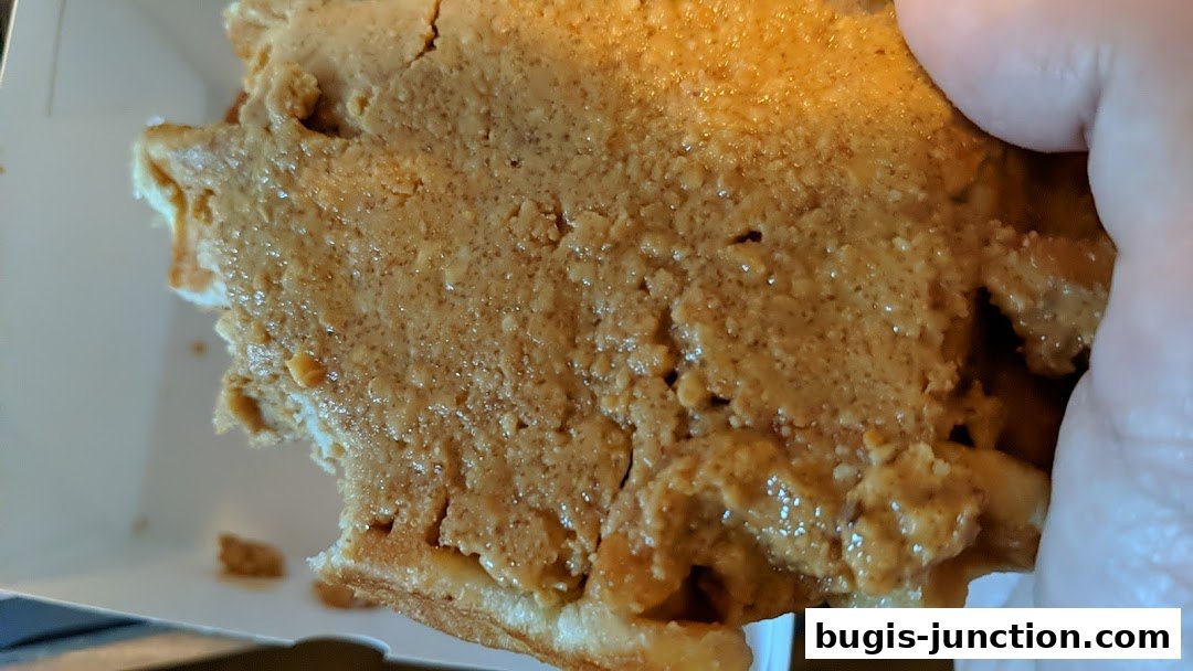 A close-up shot of a waffle generously topped with creamy peanut butter.