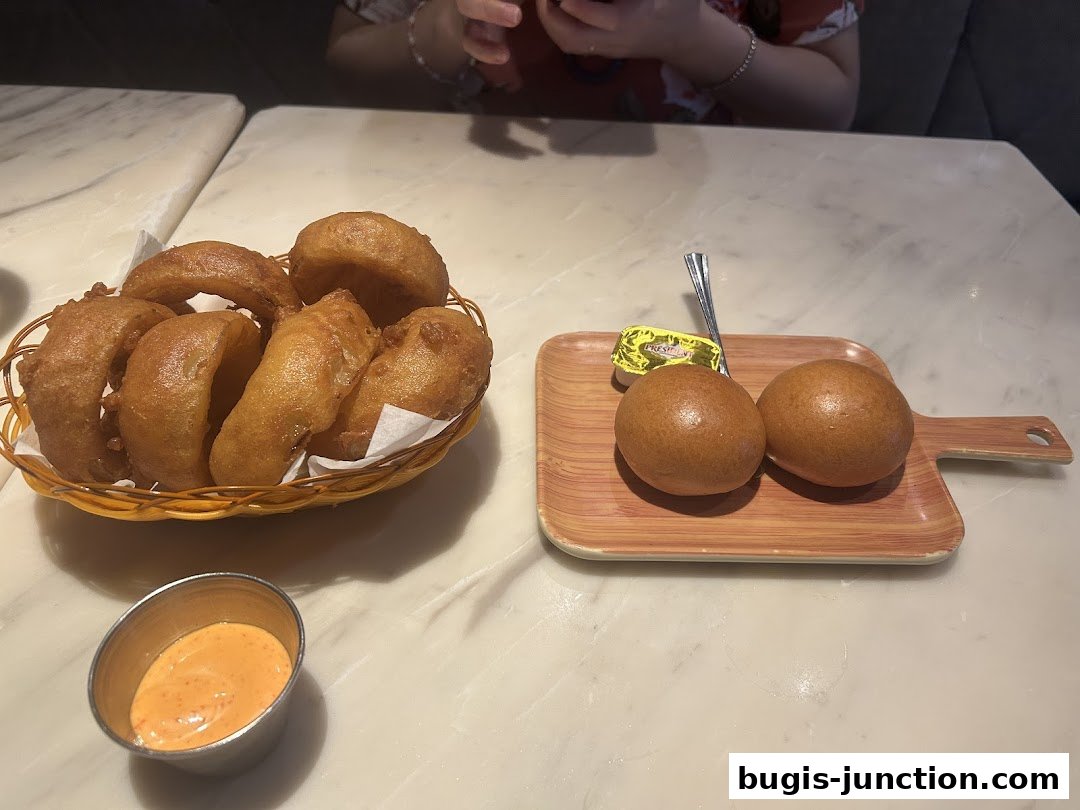 A basket of onion rings and two dinner rolls with butter are served on a table.