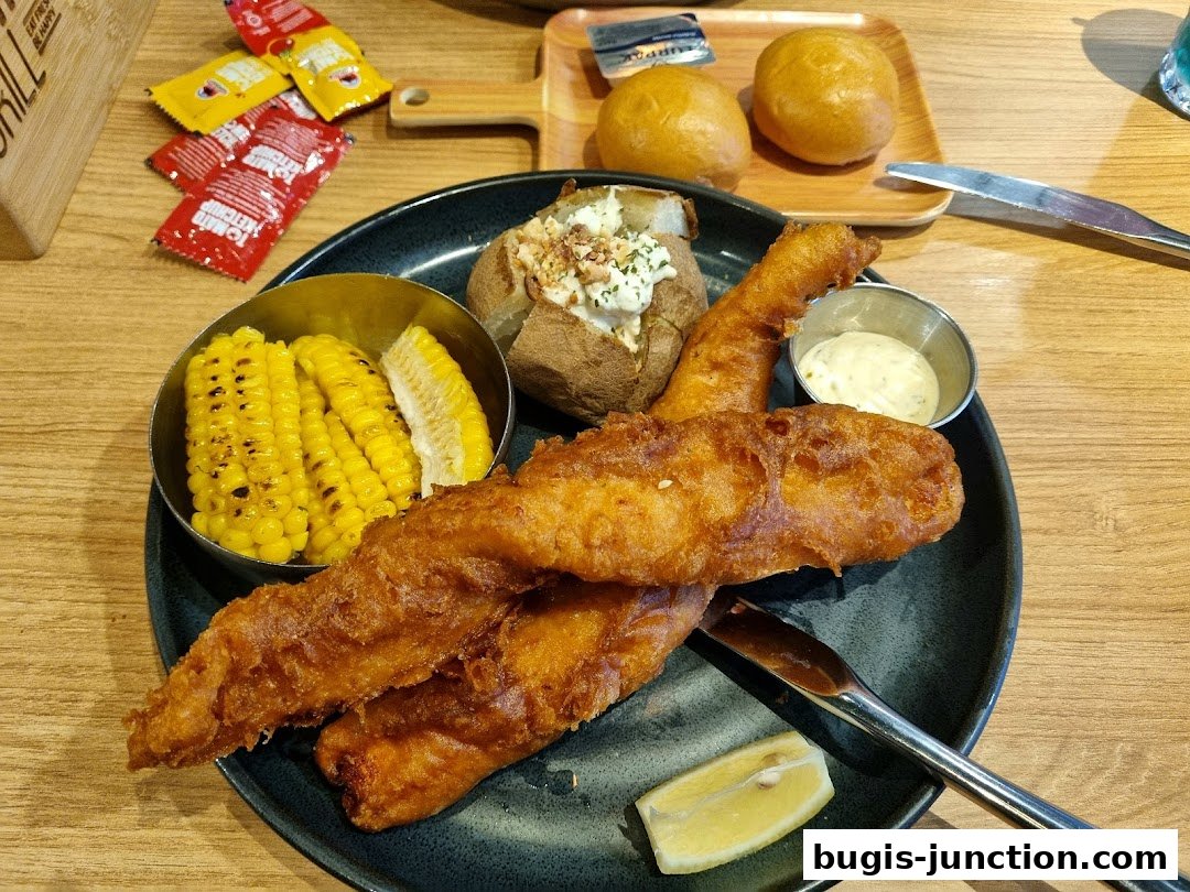 A plate of fish and chips with corn on the cob and a baked potato.