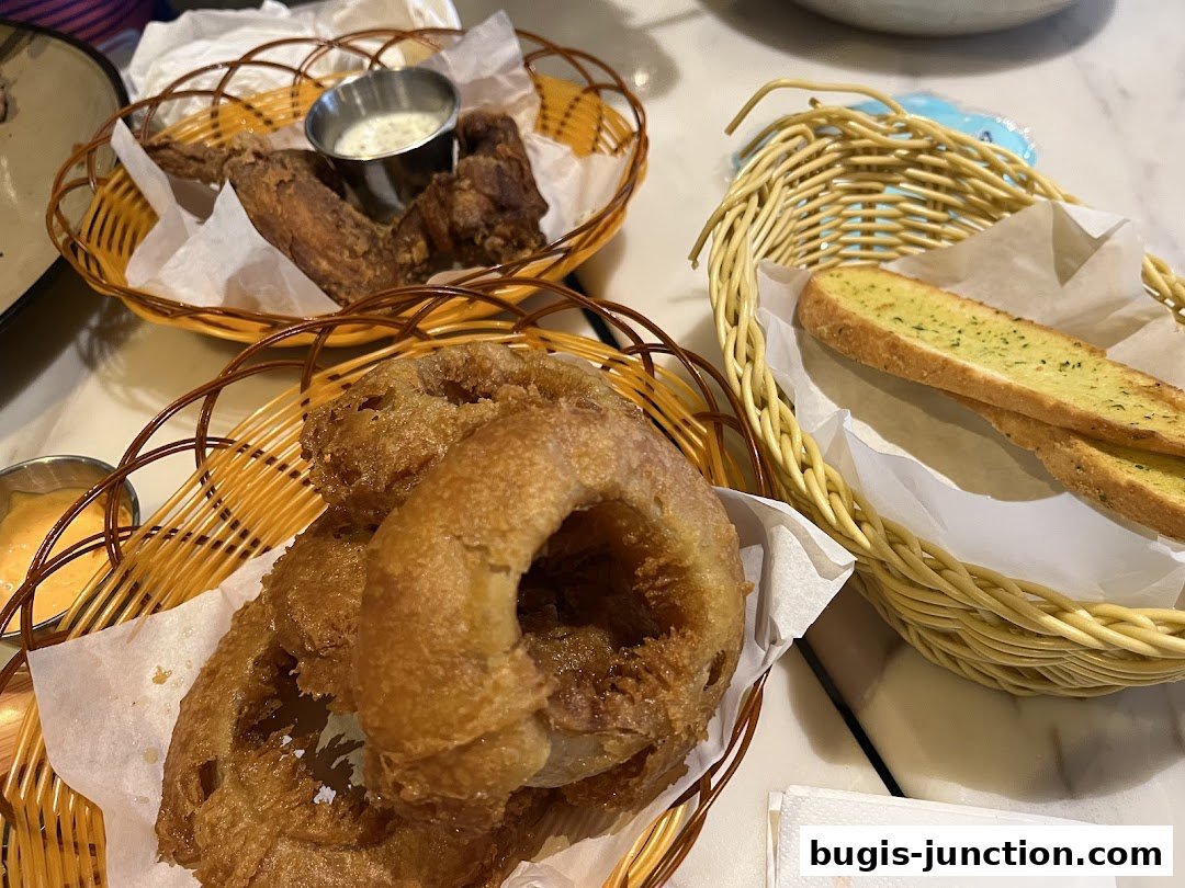 A close-up shot of fried onion rings, chicken wings, and garlic bread served in baskets.