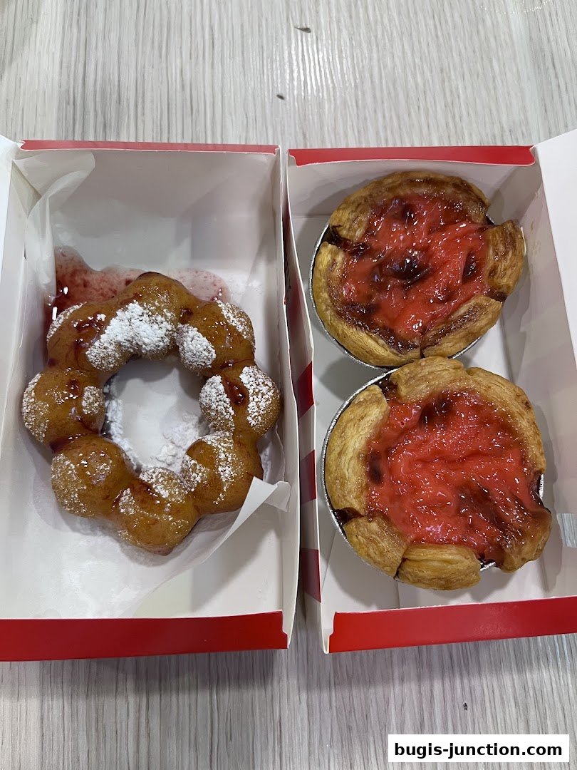 Two boxes of freshly baked pastries, one with a powdered donut and the other with two fruit tarts.