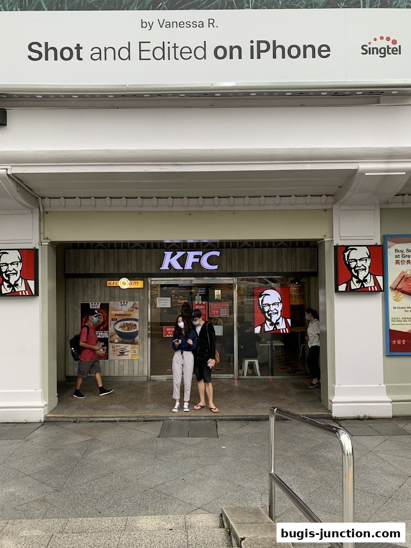 The entrance of a KFC restaurant with people standing outside.