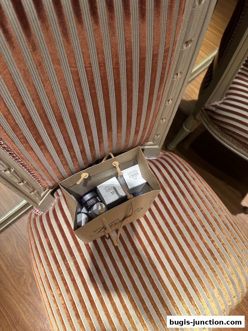 A Kiehl's shopping bag filled with skincare products rests on a striped chair.