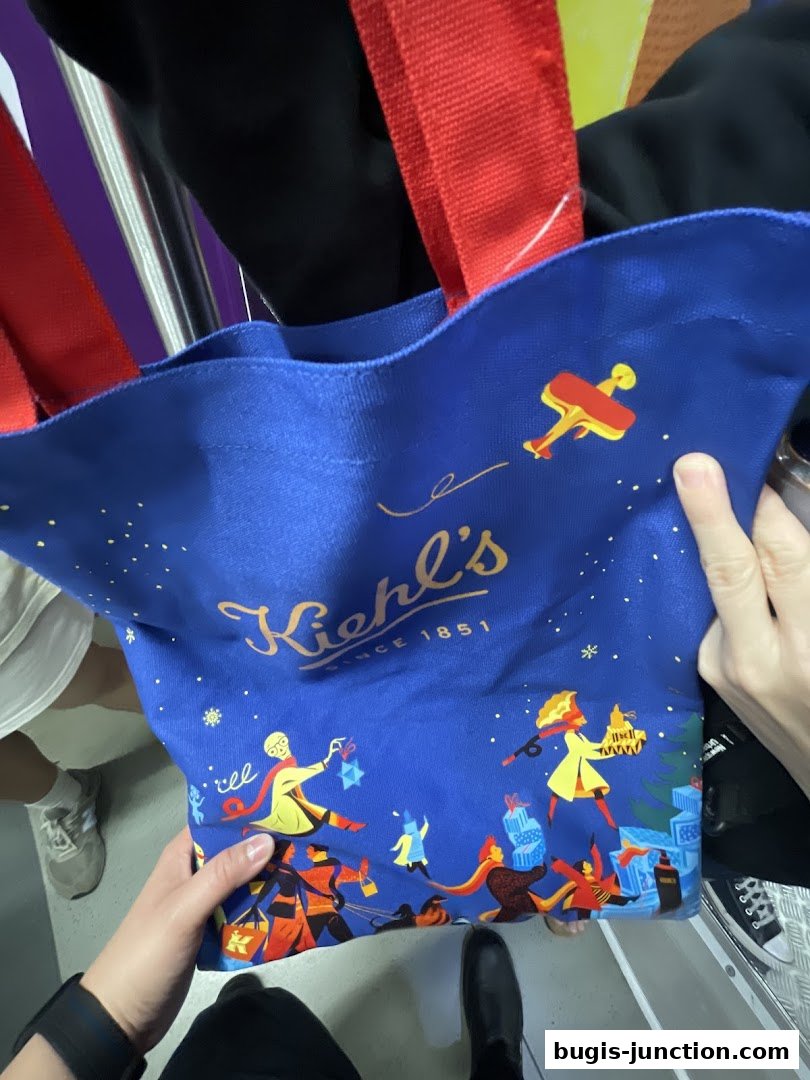 A person holds a blue Kiehl's tote bag with a festive holiday design.
