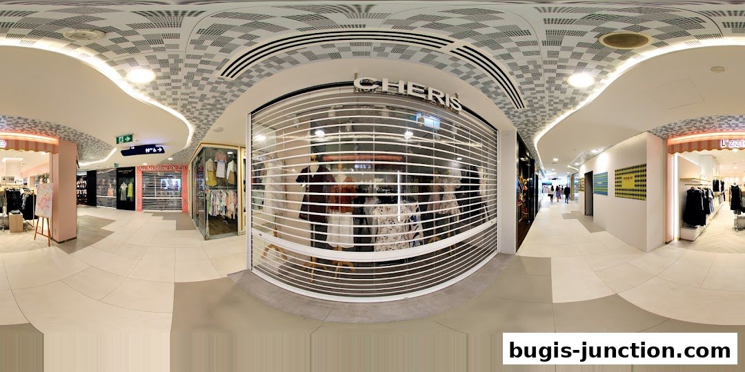 A panoramic view of a shopping mall corridor with several shop fronts visible.
