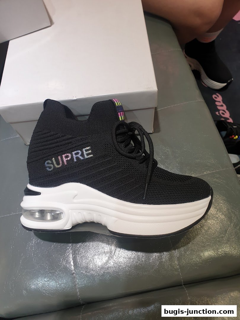 A black sneaker with a white platform sole and colorful 'SUPRE' lettering.