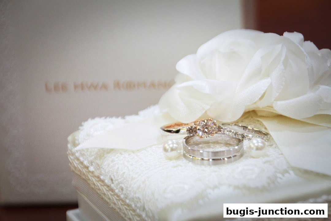 A close-up of wedding rings and pearls on a lace cushion with a floral accent.