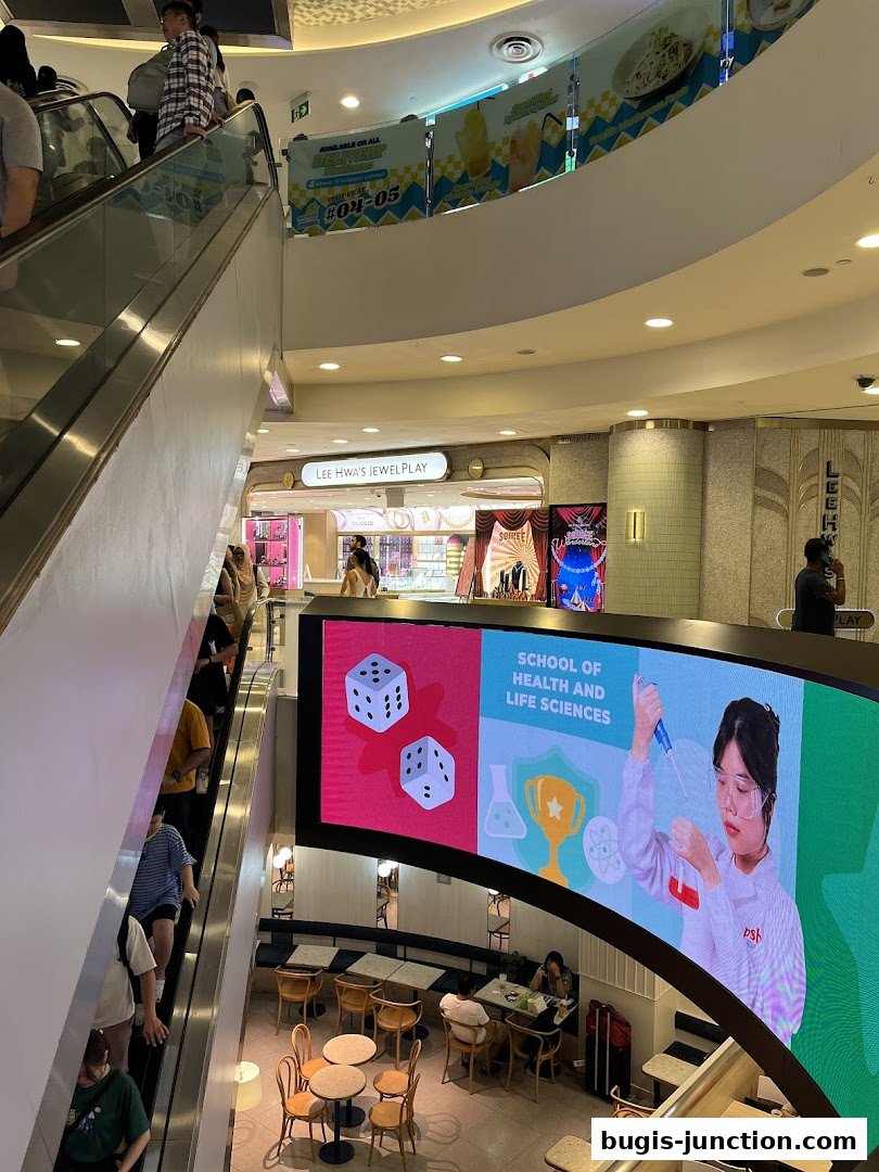 View of a shopping mall interior with escalators, a jewelry store, and a large digital screen.