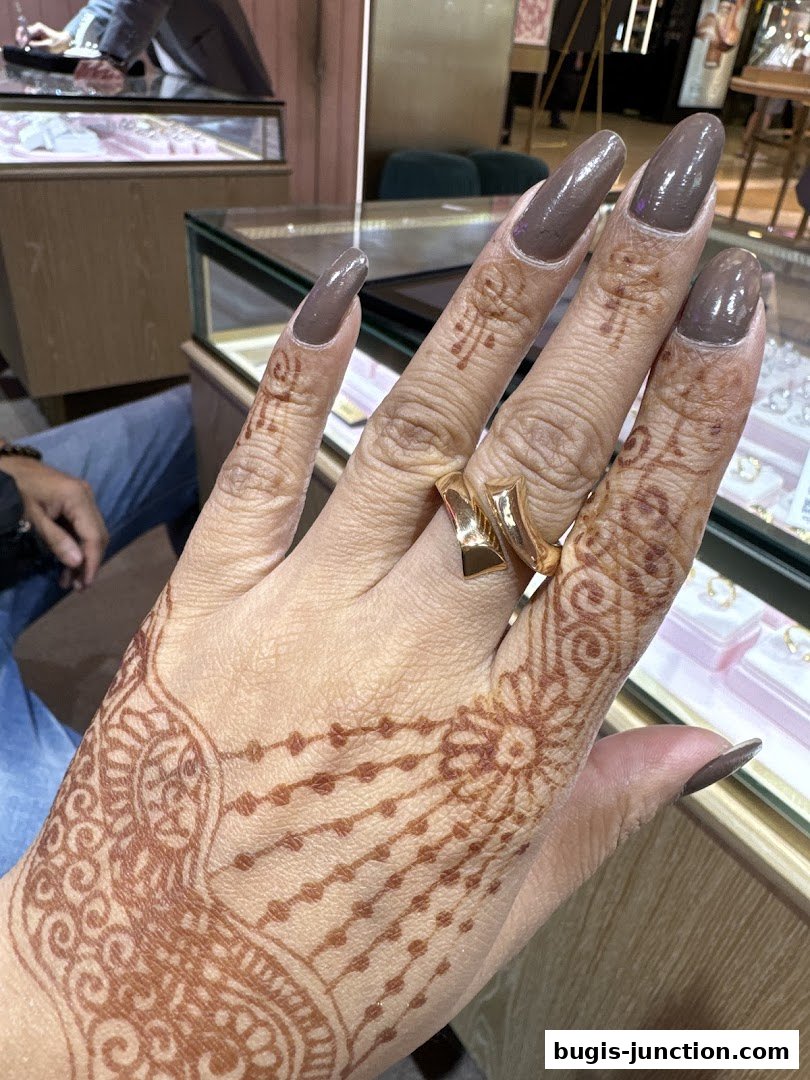 A hand with henna art and a gold ring is shown in front of a jewelry display case.