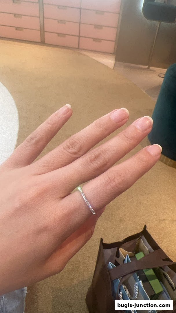 A hand wearing a diamond ring with a shopping bag in the background.