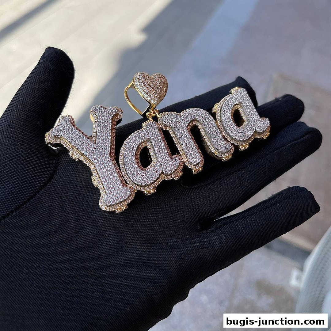 A diamond-encrusted pendant with the name 'Yana' is held on a gloved hand.