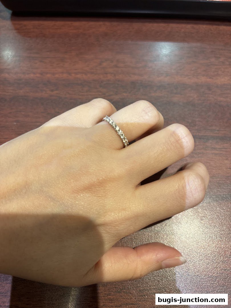 A hand wearing a diamond eternity band on a wooden surface.