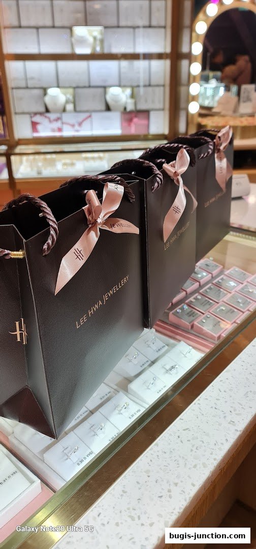 Lee Hwa Jewellery shopping bags displayed in front of a jewelry display case.