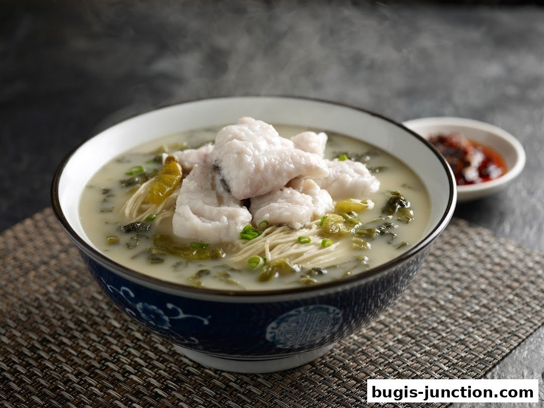 A steaming bowl of fish noodle soup with pickled vegetables and a side of chili paste.