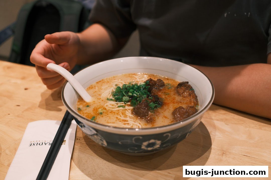 A person is about to eat a bowl of delicious noodle soup with meat and green onions.