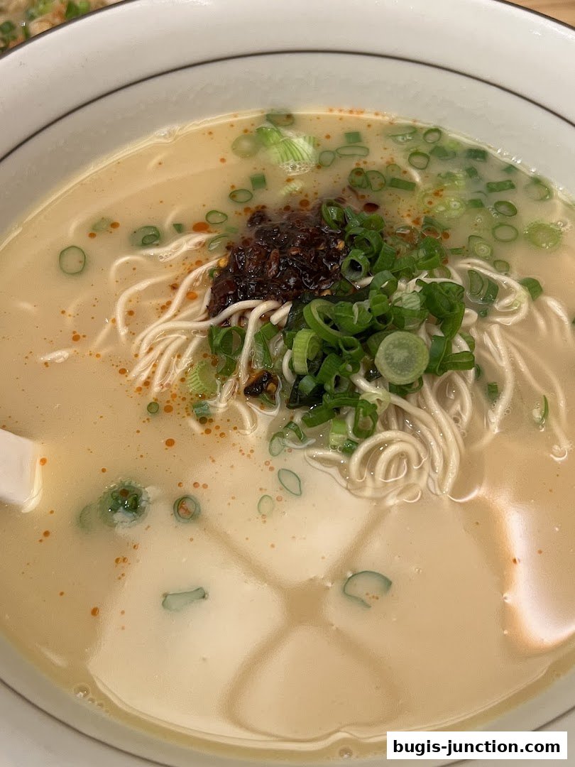 A close-up shot of a steaming bowl of noodle soup with scallions and chili paste.