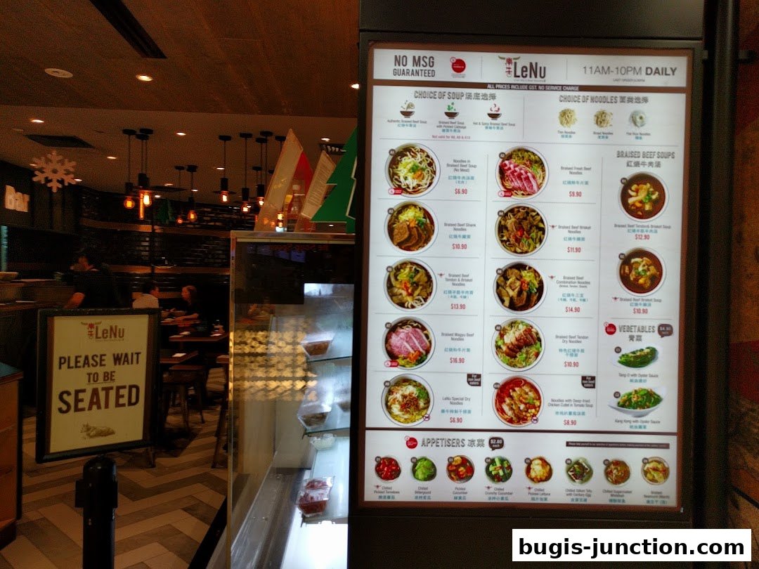 A digital menu board displays various noodle soup and appetizer options with prices.