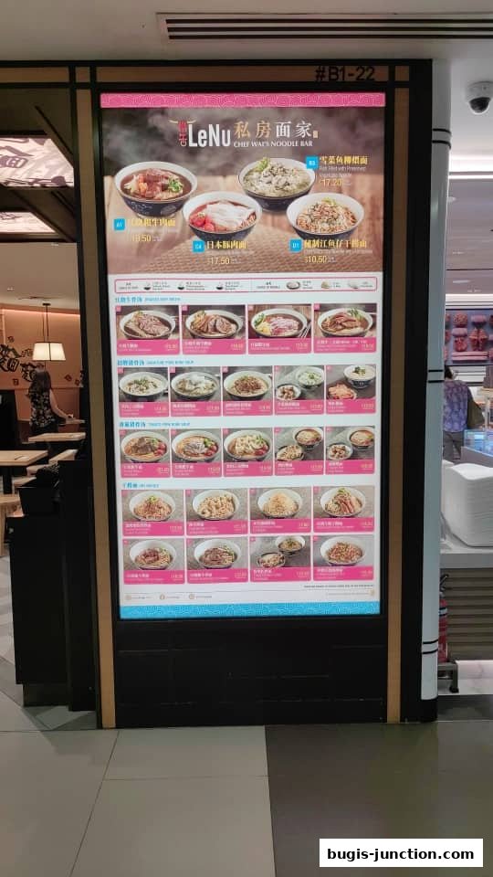 A digital menu board displaying various noodle dishes with prices at LeNu Chef Wais Noodle Bar.