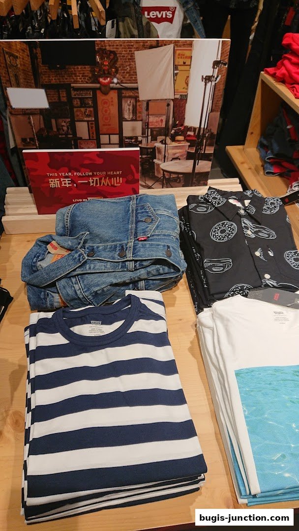 A display of folded Levi's clothing, including a denim jacket and t-shirts, with a promotional sign.