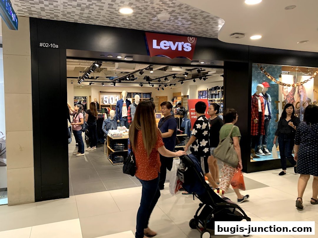 People walk past the entrance of a Levi's store displaying denim jeans and mannequins.