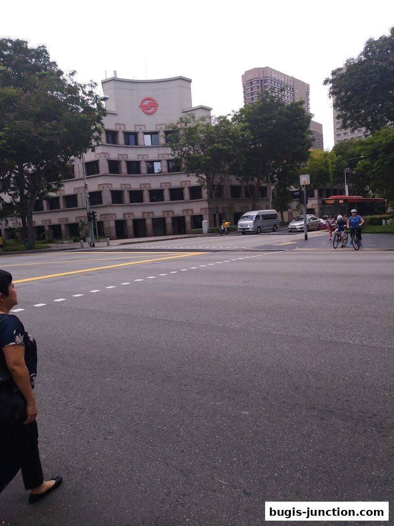 A street scene with buildings, trees, a bus, cars, and people cycling.