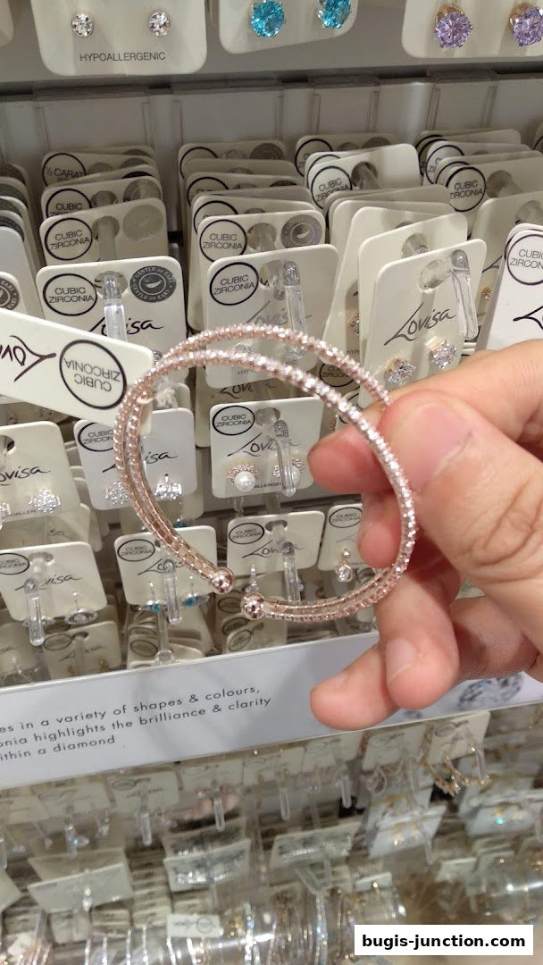 A hand holds a sparkling rose gold bracelet in front of a display of cubic zirconia earrings.