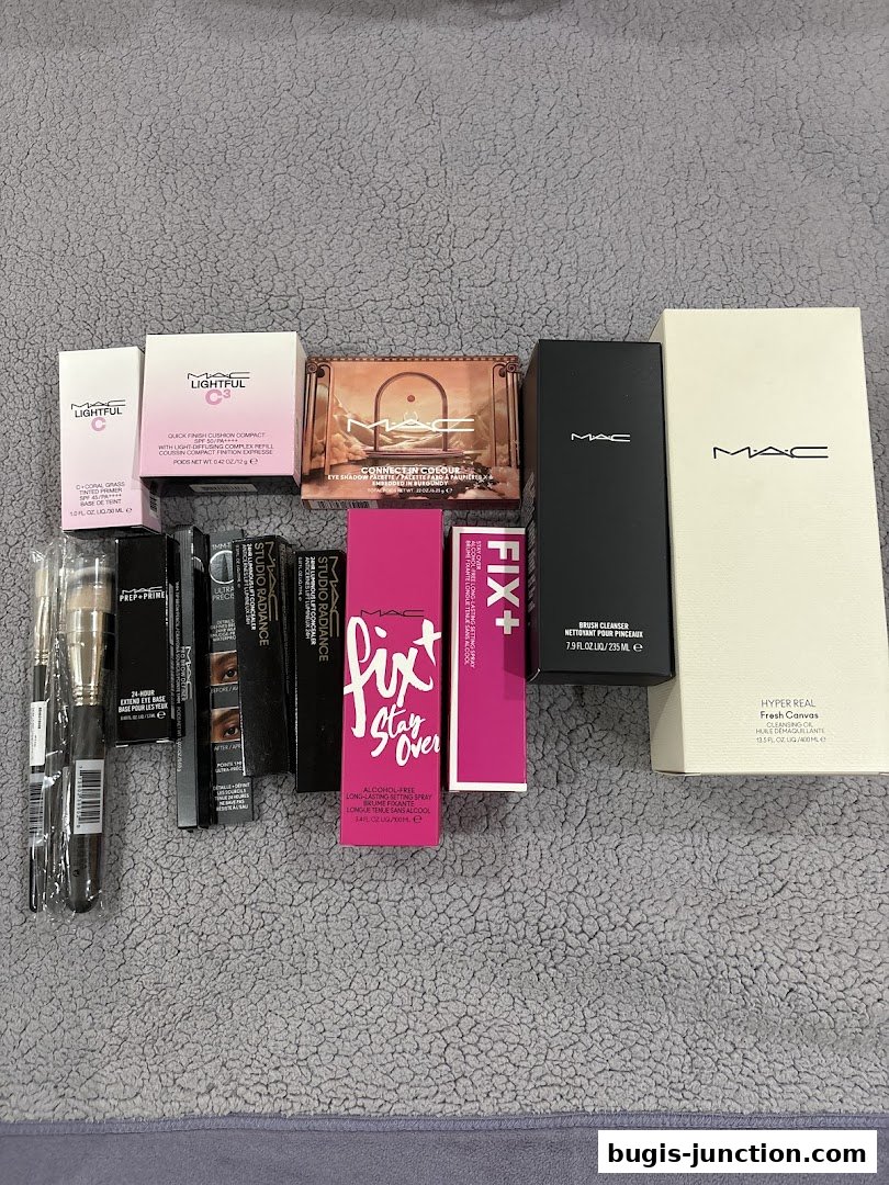 A collection of MAC Cosmetics makeup products including foundation, eyeshadow, setting spray, and brushes.