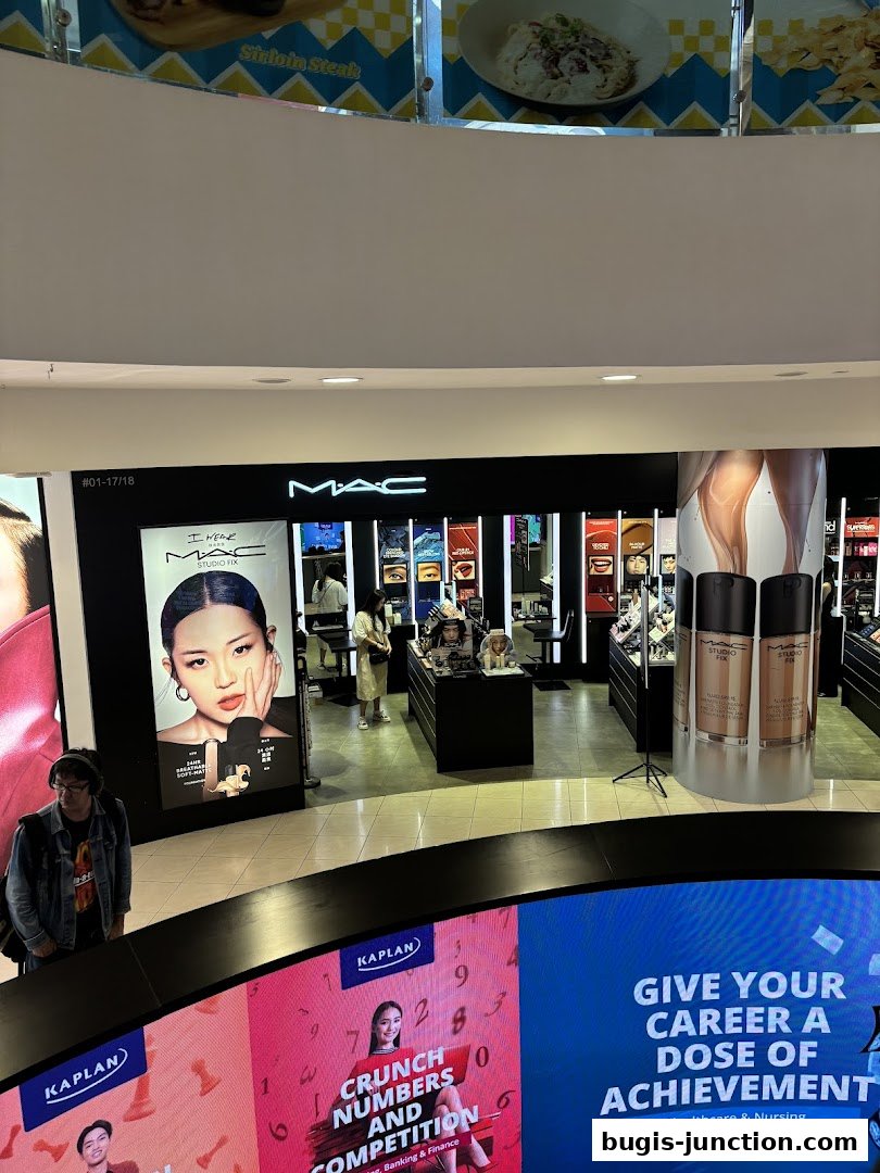 A MAC Cosmetics store in a mall, featuring makeup displays and promotional posters.
