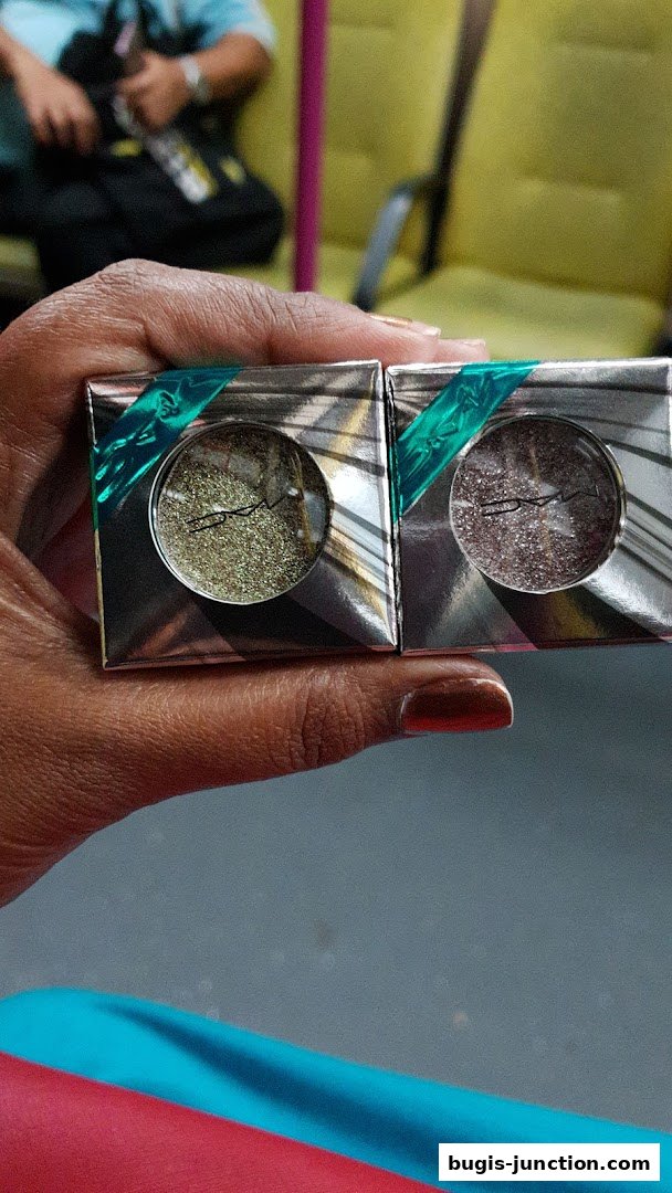 A hand holds two MAC Cosmetics eyeshadows with glittery finishes.