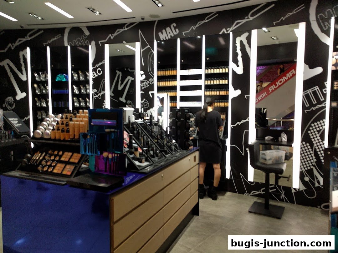 Interior of a MAC Cosmetics store with makeup displays and a staff member.
