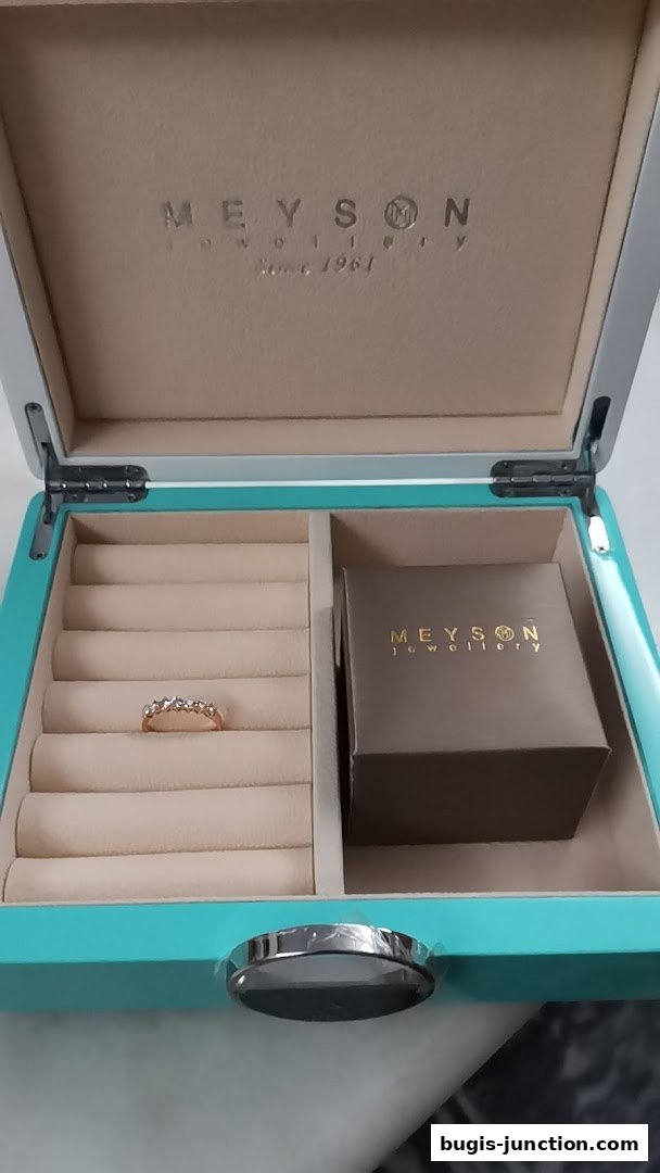 An open jewelry box with a ring and a gift box inside, branded Meyson Jewellery.