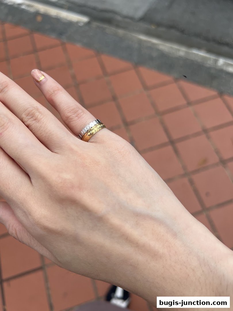 A hand wearing a gold and silver ring with diamonds, showcasing intricate design.