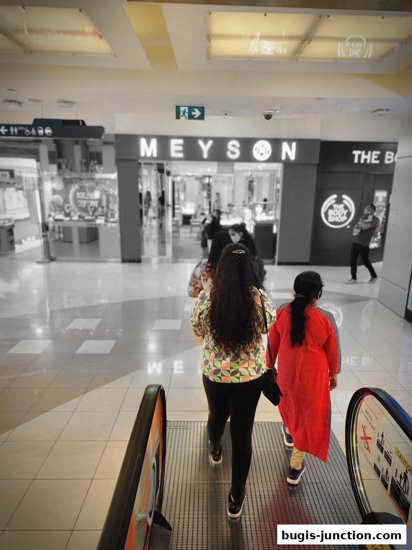 People on an escalator in a mall, passing by Meyson Jewellery and The Body Shop.