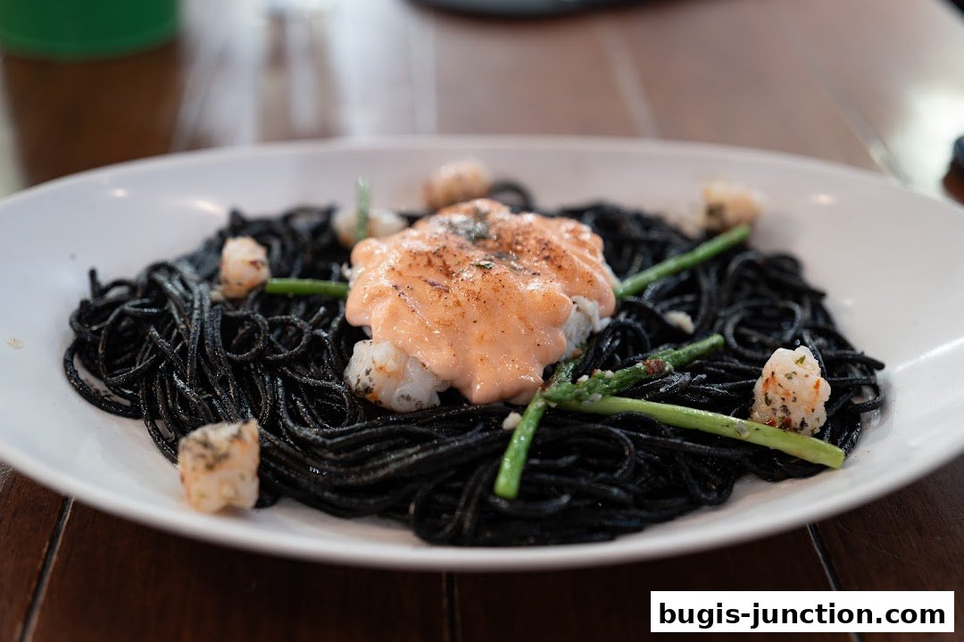 A close-up of black squid ink pasta topped with creamy salmon and shrimp, garnished with asparagus.