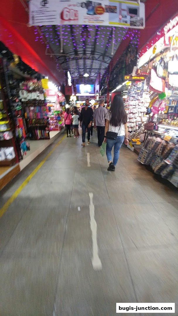 People walking through a busy market aisle with shops on either side.