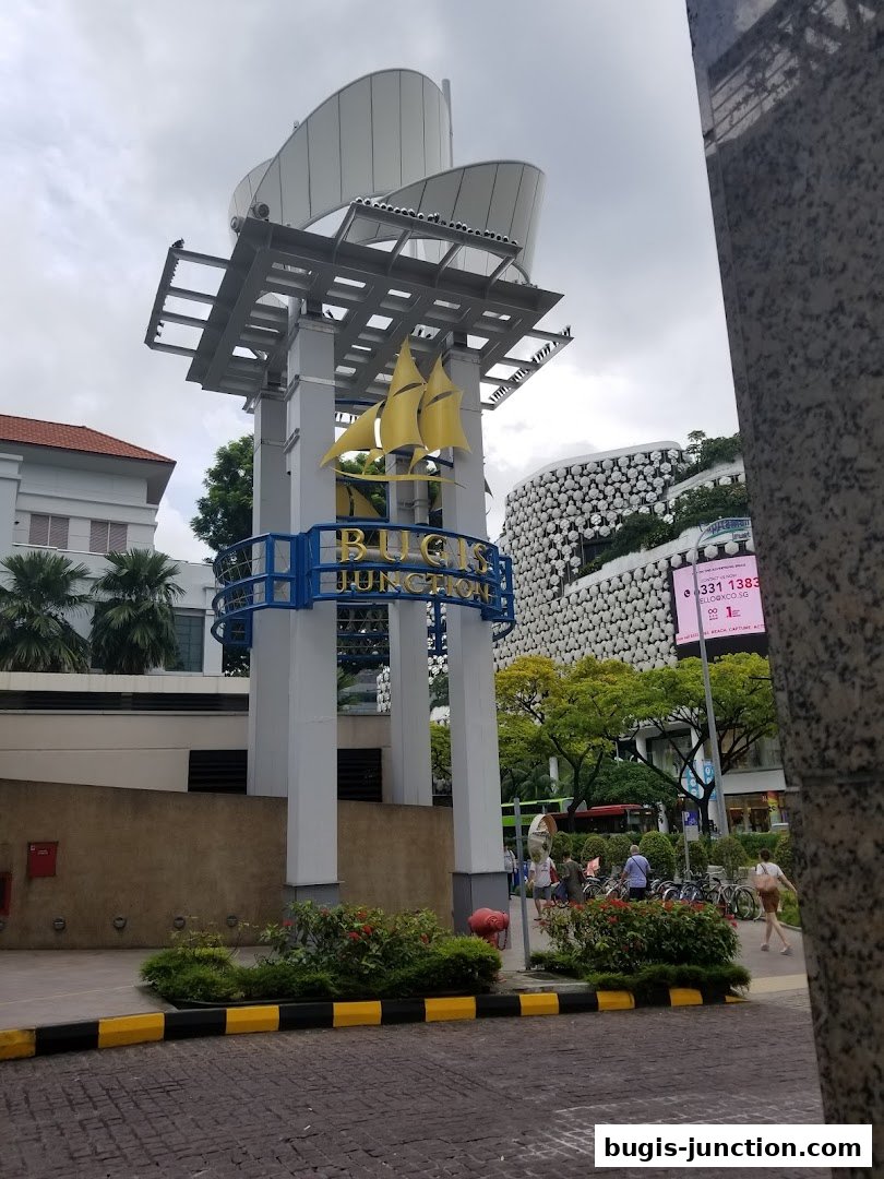 The iconic Bugis Junction sign with a sailboat emblem against a cloudy sky.